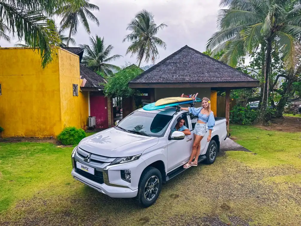 A couple standing with their pickup truck with surfboards on top, in front of a villa at Villa Mitirapa, ready for outdoor adventures in Tahiti.